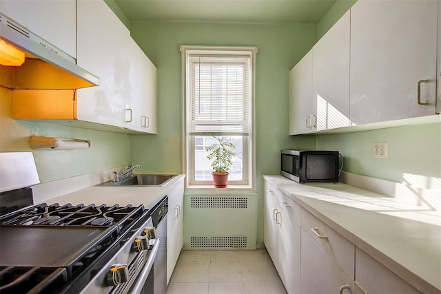 kitchen featuring appliances with stainless steel finishes, radiator heating unit, sink, white cabinets, and light tile patterned floors