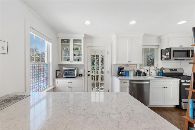 kitchen with sink, backsplash, white cabinetry, light stone countertops, and stainless steel appliances