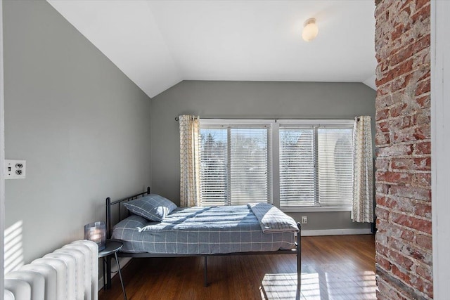 bedroom with radiator heating unit, brick wall, wood-type flooring, and lofted ceiling