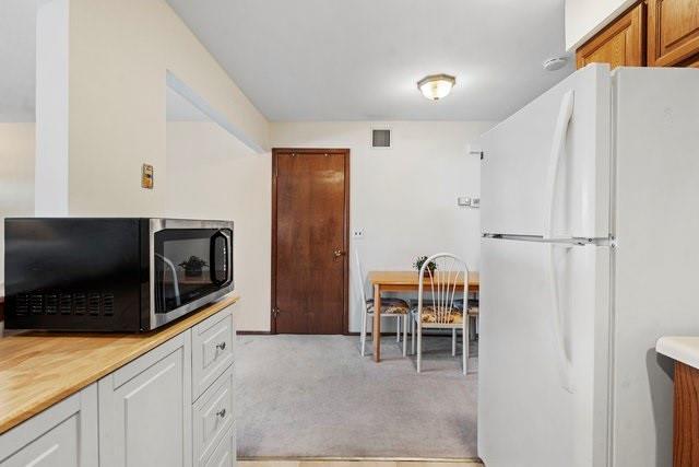 kitchen featuring light carpet, white fridge, and white cabinets