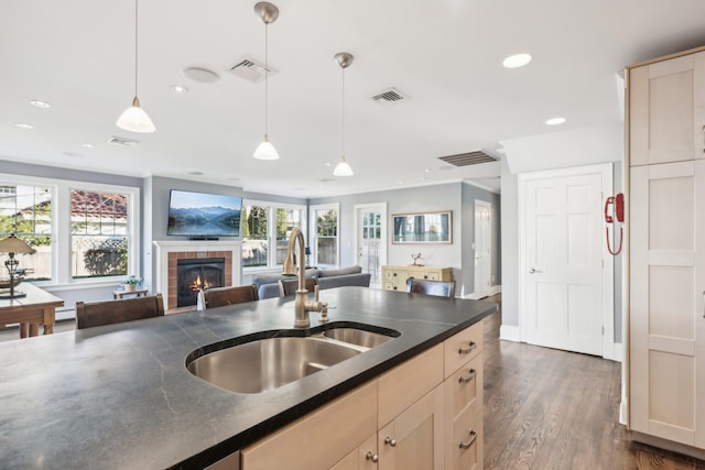 kitchen featuring dark wood-type flooring, sink, decorative light fixtures, light brown cabinets, and a tile fireplace