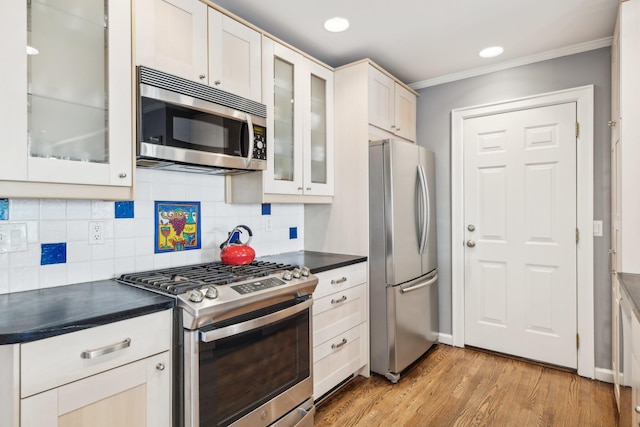 kitchen with tasteful backsplash, white cabinetry, ornamental molding, stainless steel appliances, and light hardwood / wood-style flooring