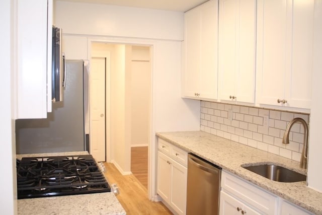 kitchen featuring dishwasher, sink, white cabinets, light stone countertops, and gas stovetop