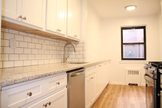 kitchen featuring light stone countertops, radiator, white cabinetry, stainless steel appliances, and sink