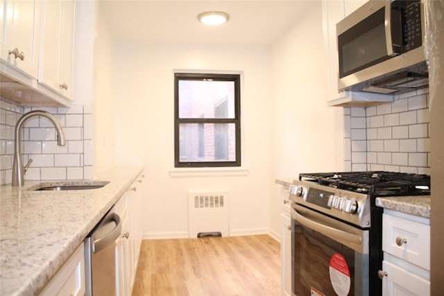 kitchen featuring radiator heating unit, sink, white cabinetry, light stone counters, and stainless steel appliances