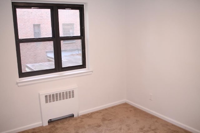 spare room with radiator heating unit and light colored carpet