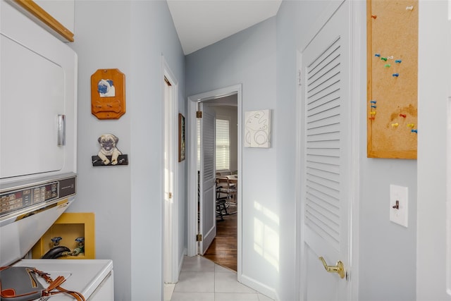 hall with stacked washer / dryer, light tile patterned flooring, and baseboards