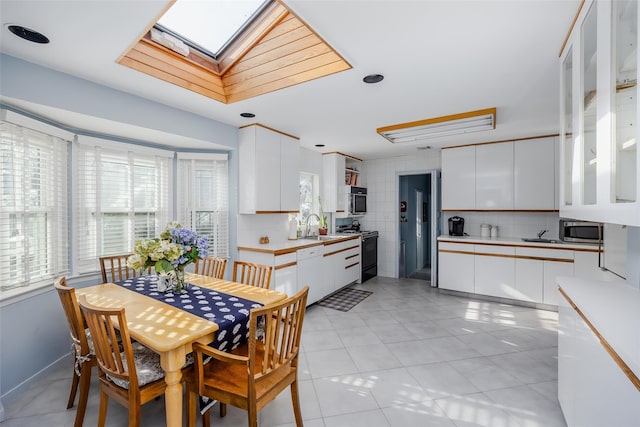 dining room featuring light tile patterned floors, a skylight, and tile walls