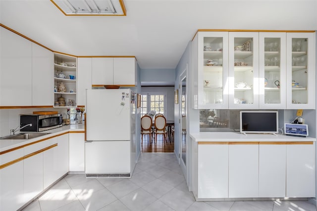 kitchen with light countertops, glass insert cabinets, freestanding refrigerator, and white cabinetry