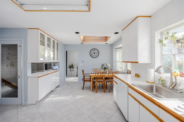 kitchen with a skylight, a sink, white cabinetry, dishwasher, and glass insert cabinets