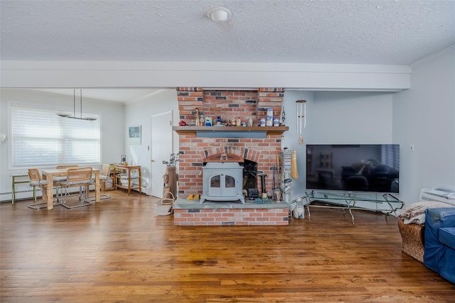 living room with a textured ceiling, wood finished floors, a wood stove, and crown molding