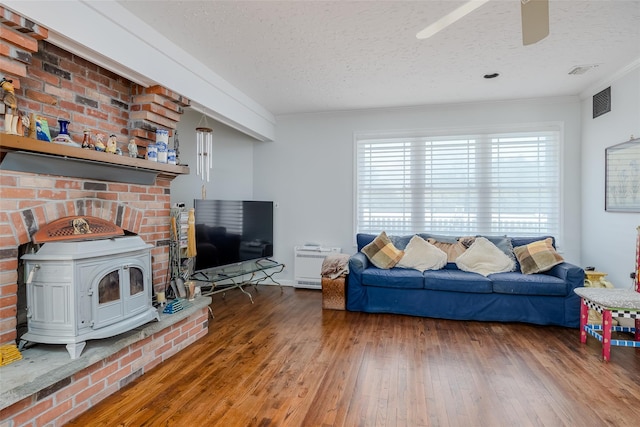 living room with a textured ceiling, wood finished floors, visible vents, a wood stove, and crown molding