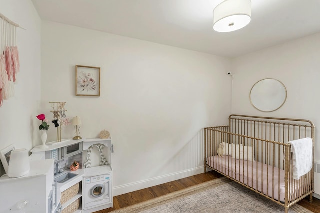 bedroom featuring washer / clothes dryer, hardwood / wood-style flooring, and a nursery area