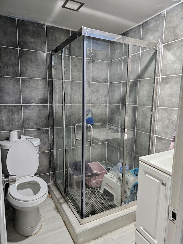 bathroom featuring toilet, a shower with shower door, tile walls, vanity, and tile patterned flooring