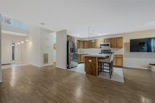 kitchen with a kitchen island, light wood-type flooring, a kitchen breakfast bar, and appliances with stainless steel finishes