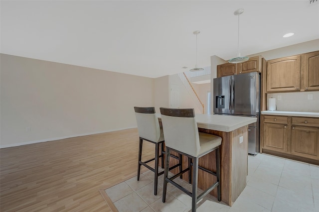 kitchen with pendant lighting, light hardwood / wood-style flooring, a center island, stainless steel refrigerator with ice dispenser, and a kitchen bar