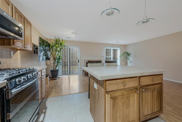 kitchen with stainless steel appliances, decorative backsplash, a kitchen island, decorative light fixtures, and light wood-type flooring