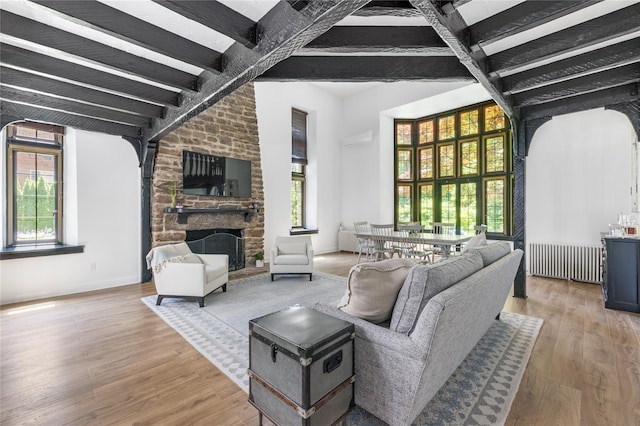 living room featuring beam ceiling, radiator heating unit, a high ceiling, a fireplace, and wood-type flooring