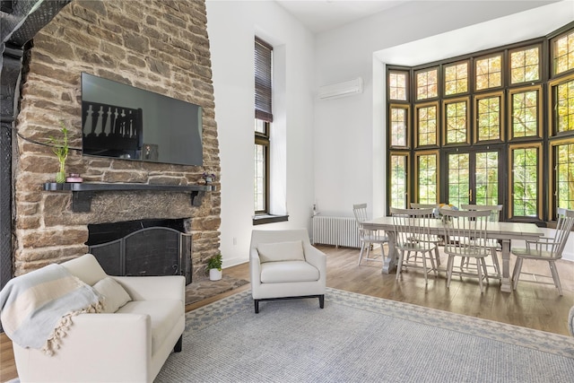 sitting room with radiator, a high ceiling, wood-type flooring, a stone fireplace, and an AC wall unit