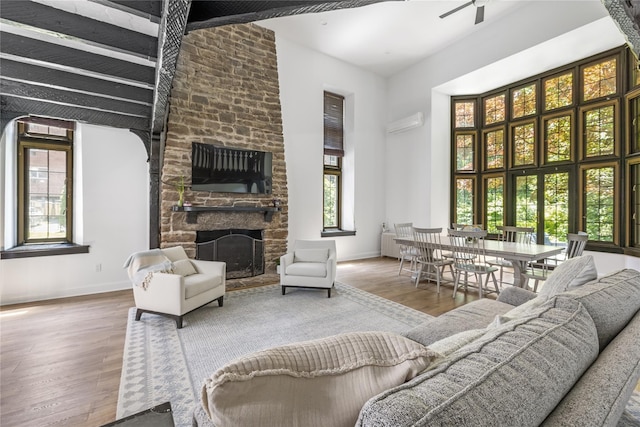 living room with a high ceiling, a stone fireplace, hardwood / wood-style floors, and ceiling fan