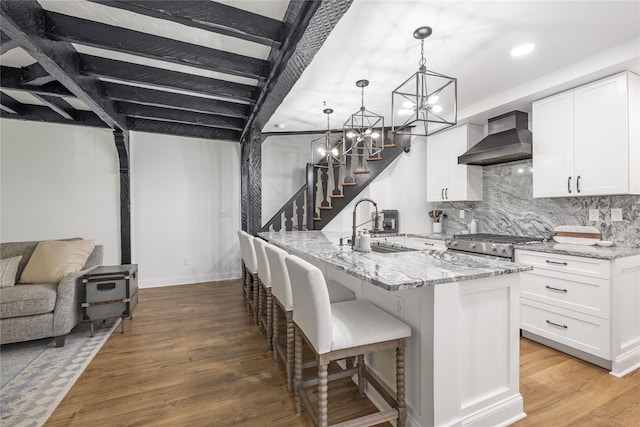 kitchen featuring white cabinetry, wall chimney exhaust hood, decorative light fixtures, and light stone counters