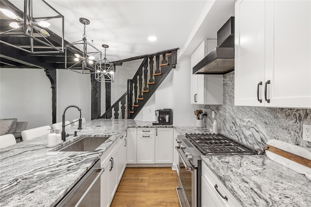 kitchen featuring wall chimney range hood, light stone countertops, white cabinets, and appliances with stainless steel finishes