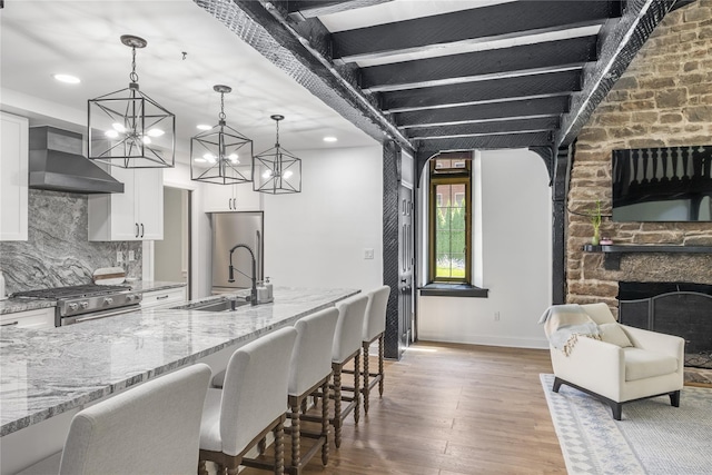 kitchen with wall chimney exhaust hood, light stone counters, a kitchen breakfast bar, pendant lighting, and white cabinets