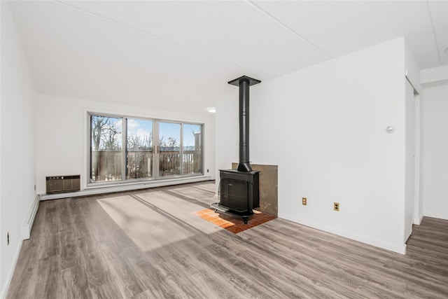 unfurnished living room with wood-type flooring, baseboard heating, a wall mounted air conditioner, and a wood stove