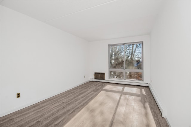 spare room featuring baseboard heating and hardwood / wood-style floors