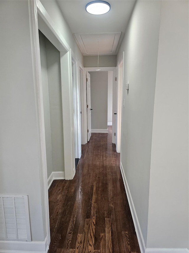 hallway featuring attic access, visible vents, dark wood finished floors, and baseboards