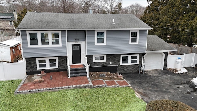 split foyer home featuring driveway, a shingled roof, stone siding, fence, and a front yard