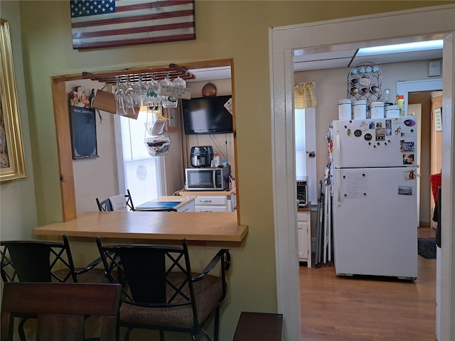 kitchen featuring kitchen peninsula, white refrigerator, hardwood / wood-style flooring, and a kitchen breakfast bar