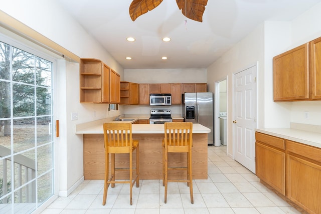 kitchen featuring a kitchen breakfast bar, kitchen peninsula, ceiling fan, sink, and stainless steel appliances