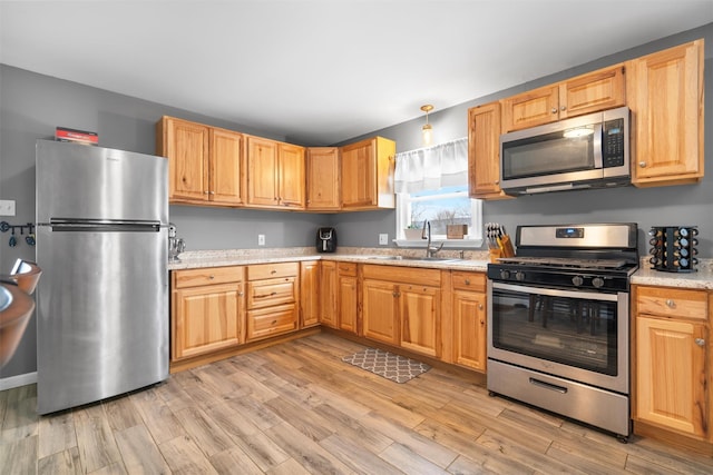 kitchen with appliances with stainless steel finishes, light stone countertops, sink, and light wood-type flooring