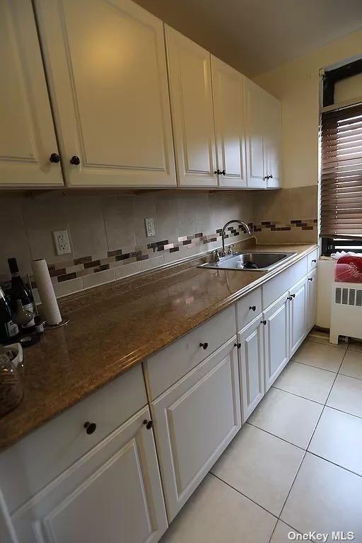 kitchen with radiator, light tile patterned floors, white cabinets, sink, and dark stone counters