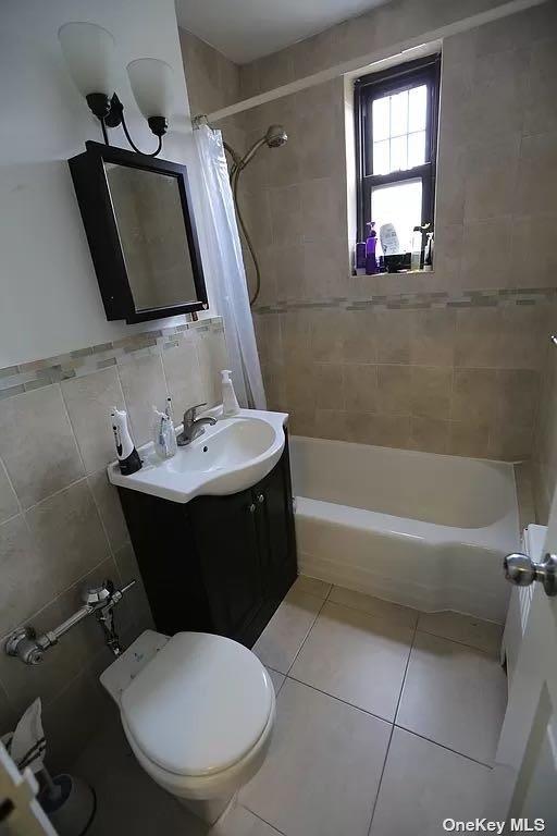 full bathroom featuring tile patterned flooring, tile walls, toilet, vanity, and shower / bathtub combination with curtain