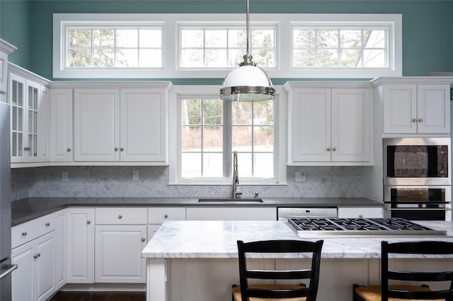 kitchen with pendant lighting, stainless steel gas stovetop, sink, a kitchen bar, and dark stone counters