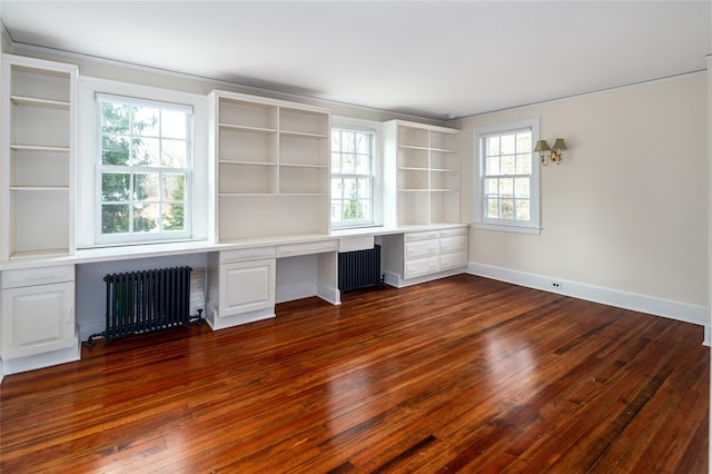 unfurnished office featuring radiator heating unit, dark wood-type flooring, built in desk, and a wealth of natural light