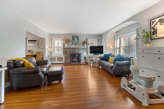 living room featuring hardwood / wood-style floors, radiator heating unit, a stone fireplace, and a wall mounted AC