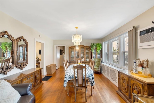 dining area featuring an inviting chandelier, radiator, light hardwood / wood-style floors, and an AC wall unit