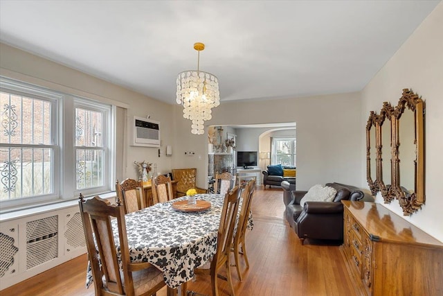 dining space featuring an inviting chandelier, a wall unit AC, and light hardwood / wood-style flooring