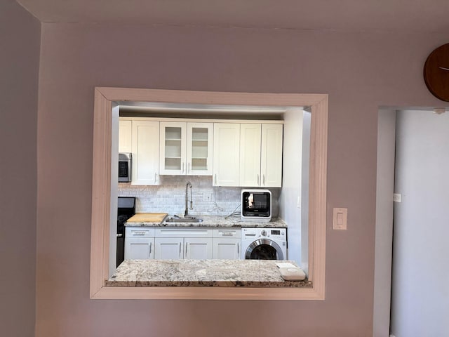 kitchen with light stone countertops, washer / clothes dryer, white cabinetry, sink, and backsplash