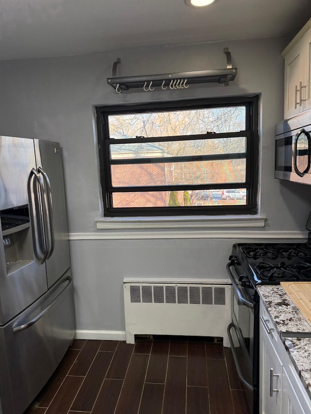 kitchen featuring white cabinetry, radiator, light stone countertops, and appliances with stainless steel finishes