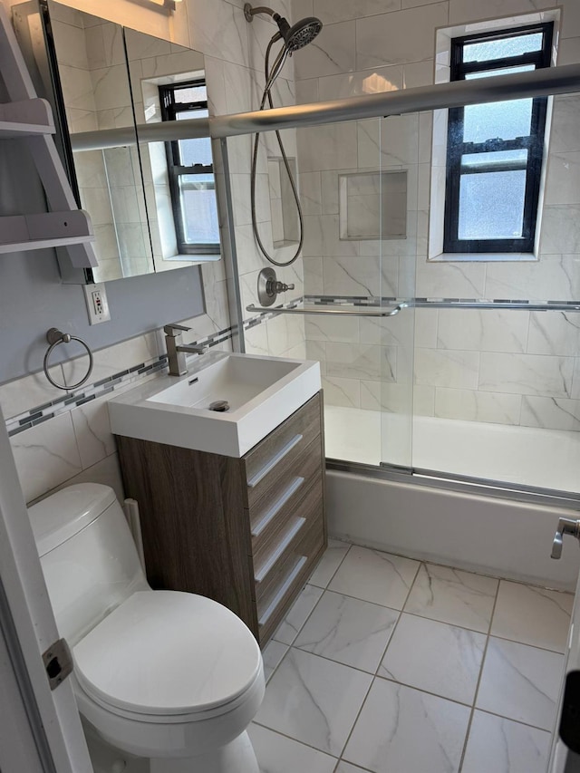 full bathroom with tile walls, combined bath / shower with glass door, vanity, and toilet