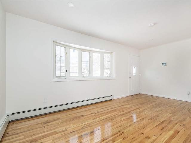 spare room featuring baseboards, a baseboard heating unit, and light wood-style floors