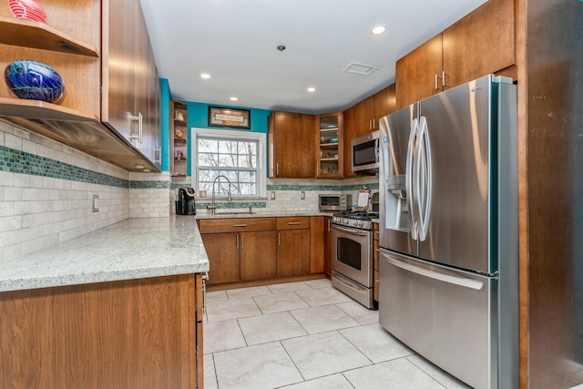 kitchen featuring sink, tasteful backsplash, light tile patterned floors, appliances with stainless steel finishes, and light stone countertops