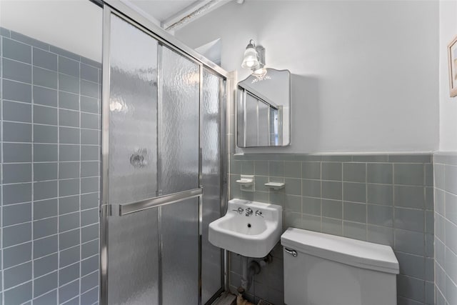 bathroom featuring tile walls, sink, a shower with shower door, and toilet