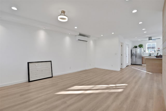 interior space featuring a wall mounted AC, ceiling fan, and light hardwood / wood-style flooring