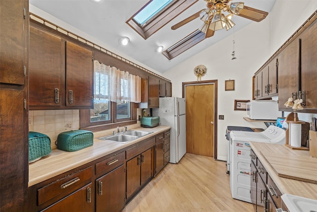 kitchen featuring white appliances, washing machine and dryer, decorative backsplash, sink, and lofted ceiling with skylight