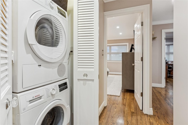 laundry area featuring crown molding, stacked washer and clothes dryer, and wood-type flooring